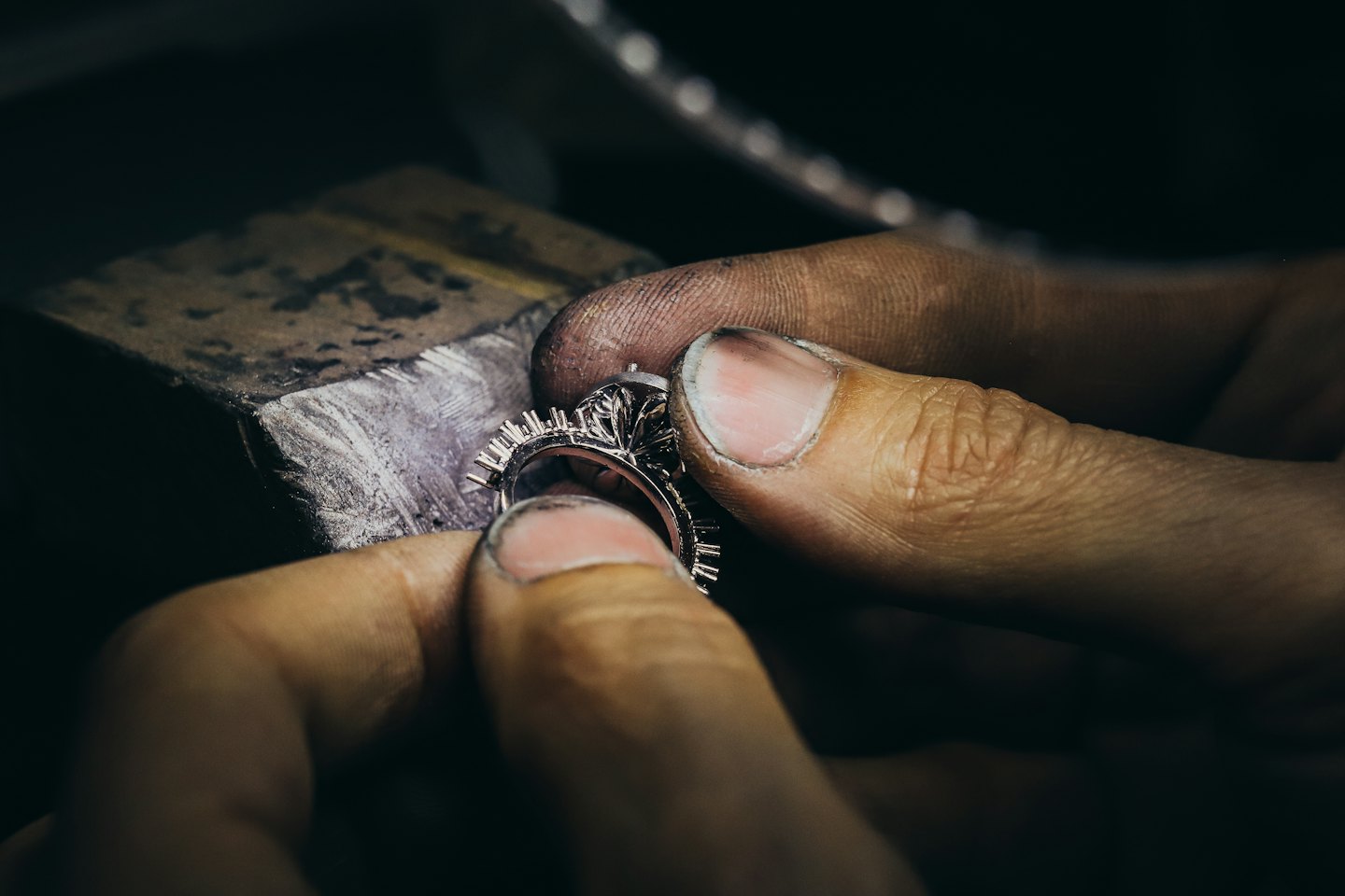 Artisan's hands setting stones in a silver ring on a workbench.