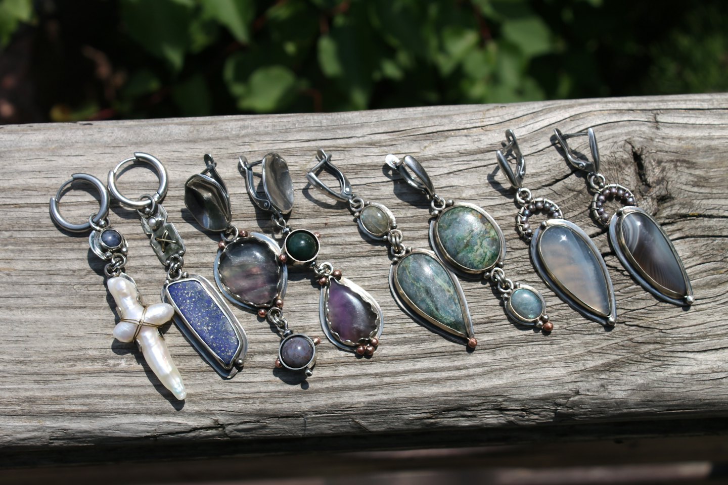 Handcrafted gemstone earrings and pendants displayed on a wooden plank.